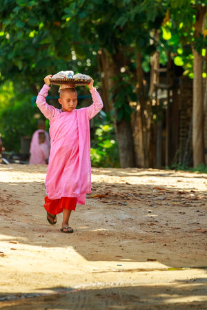 Bagan/Myanmar-October 4th 2019: A Burmese female novice walks to donate food in the morning by placing a basket on the head.のeditorial素材