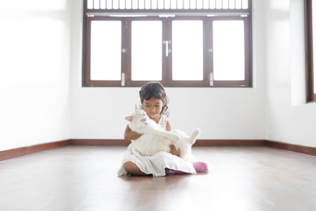 A cute Asian girl is holding her white cat sitting on the floor inside a white painted house.の写真素材