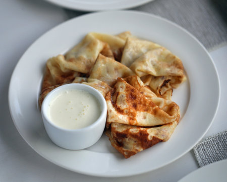 Macro photo of thin delicious pancakes with vanilla cream on a white plateの写真素材
