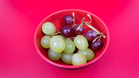 Fresh red and green grapes in a bowl isolated on pink background. Selective focus on the fresh red grapes.の写真素材
