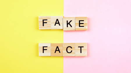 A tiles of word forming word  fact and fake on a yellow and pink background. Selective focus on the word fake and fact.の写真素材