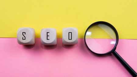 Search Engine Optimization ranking concept, abbreviation SEO on the wooden dice as an idea of promote traffic to website. Selective focus on wooden dice, magnifying glass and a mouse isolated pink and yellow background.の写真素材
