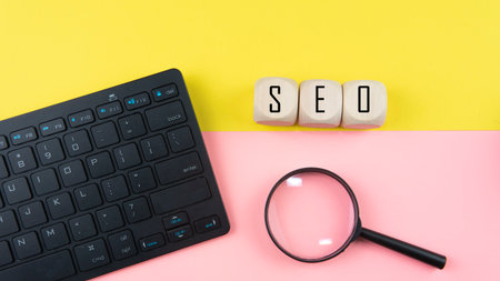 Search Engine Optimization ranking concept, abbreviation SEO on the wooden dice as an idea of promote traffic to website. Selective focus on wooden dice, magnifying glass and a mouse isolated pink and yellow background.の写真素材