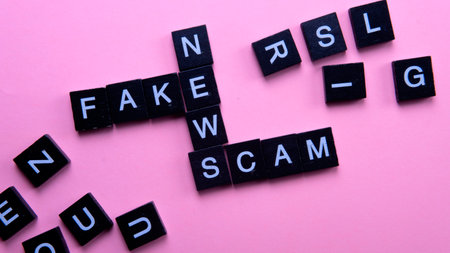 A group of scrable tile forming word scam fake news. Selective focus on the tiles isolated on pink backgroundの写真素材