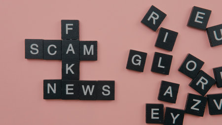 A group of scrable tile forming word scam fake news. Selective focus on the tiles isolated on pink backgroundの写真素材