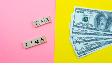 Selective focus on a word tile forming a tax time on a pink and yellow backgroundの写真素材