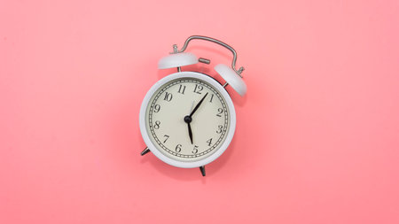 Selective focus on a white alarm clock on a pink background. A fallen white alarm clock showing how...