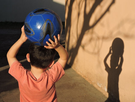 Little boy holding a soccer ball on his head and looking at the shadowの写真素材
