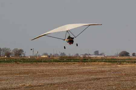 Hang glider taking off from a field during a sunny day