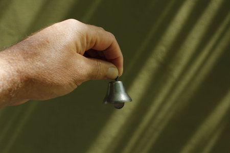 Hand ringing a bell on a green background. Close-up.