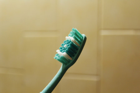 Toothbrush with green bristles on a beige background.