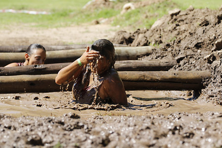 Female athlete wiping mud from her face while crossing muddy water obstacle duringobstacle course...