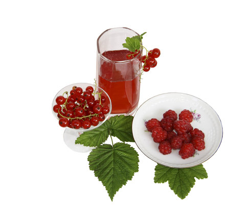 A glass with juice, a raspberry on a saucer and a red currant on a white background の写真素材
