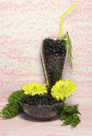 The glass glass and a vase with bilberry berries on a pink background are decorated by colours and a green branch の写真素材