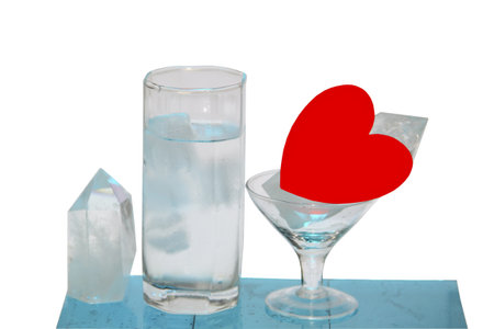 A glass of water with cubes of ice a crystal and heart on a white backgroundの写真素材