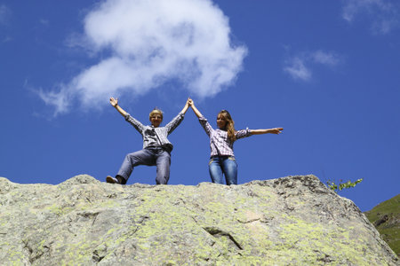 Happy mother and daughter standing on a huge rock, raising his hands upの写真素材