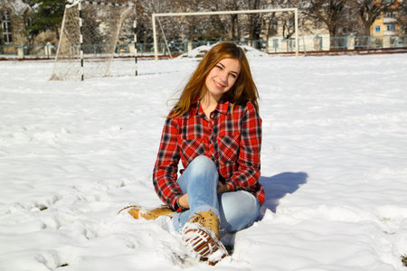 Happy young girl sitting on the snow in the park on a sunny winter dayの写真素材