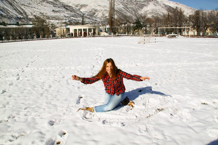 Happy young girl sitting on the snow in the park on a sunny winter dayの写真素材