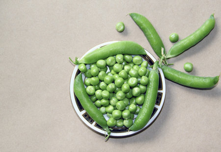 Green pea pods on a plate on a brown background, top view
