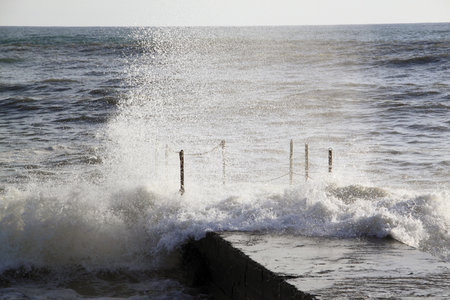 Sea waves breaking on a breakwater with sea foam and spraysの写真素材