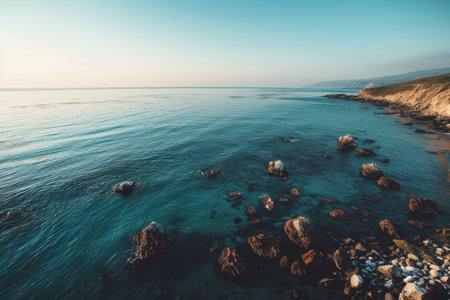 A serene coastal landscape showcases calm waves reflecting the sunset hues, with smooth rocks scattered along the shoreline in California, creating a peaceful atmosphere.の素材