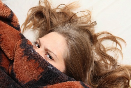 	Young girl peeking out from under the blanketの写真素材