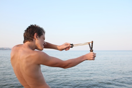 	young boy shooting from a slingshot on the sea