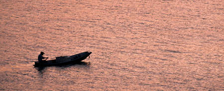 Shadows of the fishermen paddle back to the shore in the evening when the sun's rays reflect the glittering surface.の写真素材