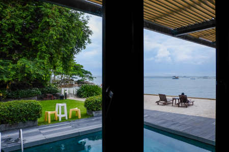 The view from the glass room overlooks the swimming pool, garden, chairs and the vast sea