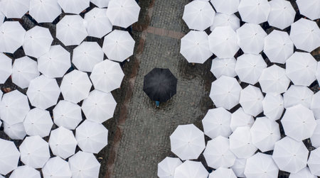 A single dark umbrella is surrounded by many white umbrellas, conceptual, standing out, wallpaper