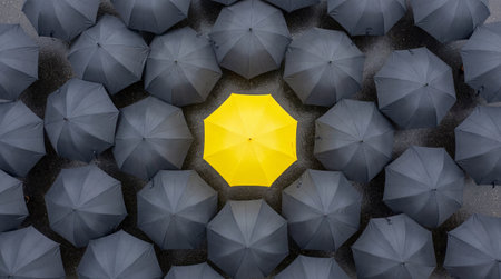Unique yellow umbrella surrounded by dark parasols in rain. Stand out from crowd concept wallpaper....