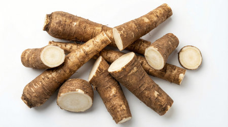 Assortment of fresh burdock roots, some whole and some sliced, arranged casually on bright white...