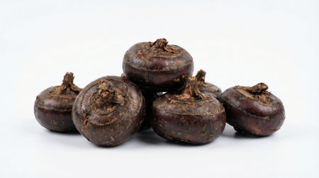 Small pile of fresh, dark brown water chestnuts with papery skin, stacked on a clean white...