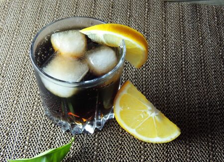 Cocktail with cola and ice on wooden table. in a glass with a cocktail, put a slice of lime