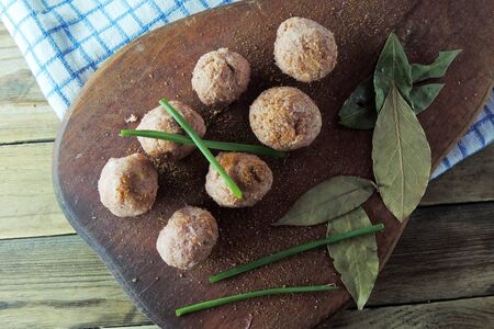 Raw meatballs in bowl with ingredients on wooden background