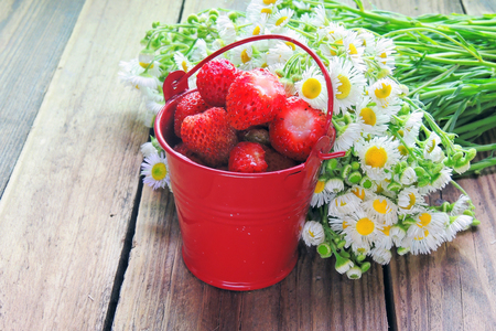 Strawberries in a bucket and a bouquet of chamomilesの写真素材
