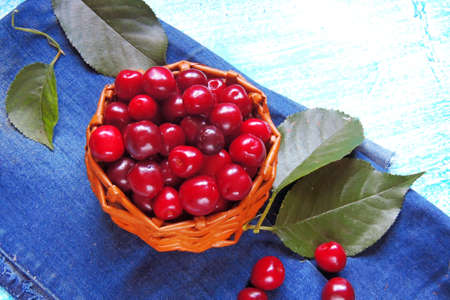 Ripe cherries in basket on old wooden table on countryside against summer foliage in sunlight