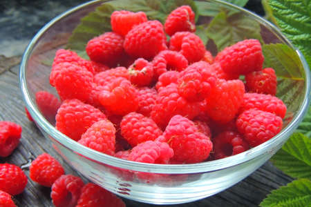 Close-up of a white plate with fresh forest raspberries, which stands on a gray wooden bench....