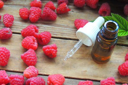 A bottle of raspberry seed oil with raspberries on a dark background