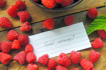 Close-up of a white plate with fresh forest raspberries, which stands on a gray wooden bench....