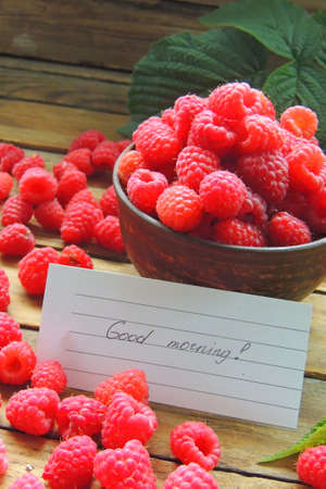 Close-up of a white plate with fresh forest raspberries, which stands on a gray wooden bench....