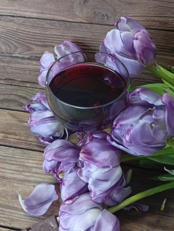 A glass of red wine and purple tulips on a wooden backgroundの写真素材