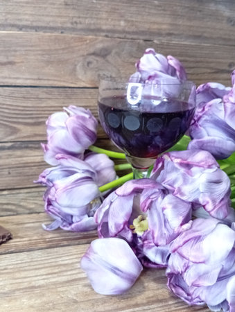 A glass of red wine and a bouquet of purple tulips on a wooden backgroundの写真素材