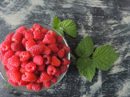 Ripe raspberries in a glass bowl on a wooden background