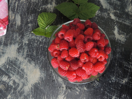 Ripe raspberries in a glass bowl on a wooden background
