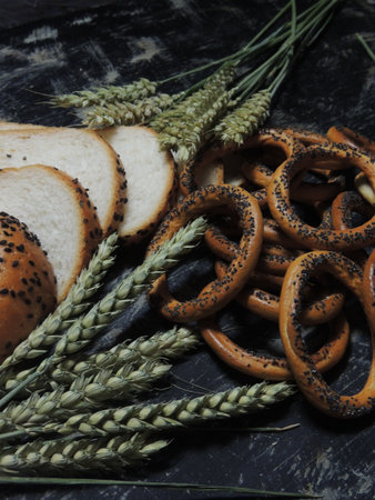 Bread with poppy seeds and spikelets of wheat on black backgroundの写真素材