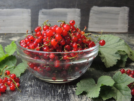 Red currant in a glass bowl on a wooden background with leaves