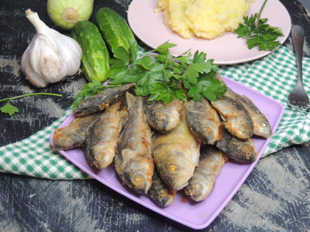 Fried fish with garlic and parsley on a plate on a wooden backgroundの写真素材