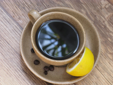 cup of coffee with a lemon on a saucer and grainsの写真素材