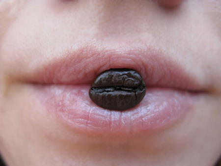 Woman holding coffee beans in mouth grain of coffee on lipsの写真素材